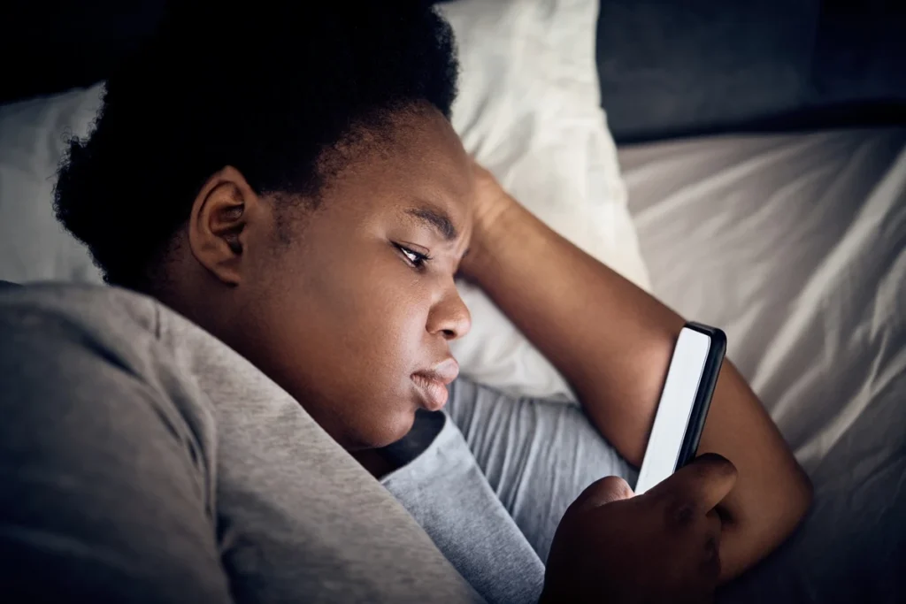 Imagem mostra mulher negra olhando o celular na cama - Entenda por que assistir vídeos acelerados prejudica o seu cérebro - Metrópoles