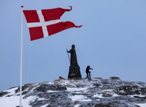 Um homem caminha enquanto a bandeira dinamarquesa tremula ao lado da estátua de Hans Egede antes...
