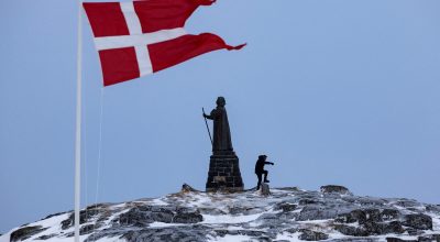 Um homem caminha enquanto a bandeira dinamarquesa tremula ao lado da estátua de Hans Egede antes...