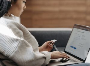Woman sitting on a couch, shopping online using a laptop and a credit card.