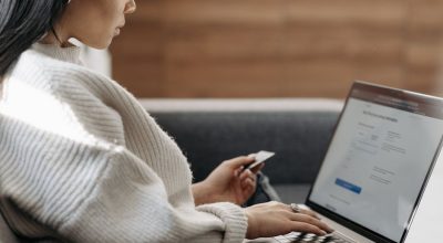 Woman sitting on a couch, shopping online using a laptop and a credit card.