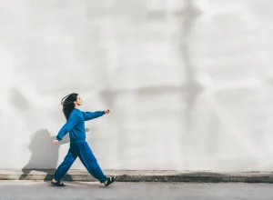 Mulher jovem de roupa azul caminhando em frente à parede branca - Metrópoles