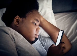 Imagem mostra mulher negra olhando o celular na cama - Entenda por que assistir vídeos acelerados prejudica o seu cérebro - Metrópoles