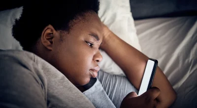 Imagem mostra mulher negra olhando o celular na cama - Entenda por que assistir vídeos acelerados prejudica o seu cérebro - Metrópoles